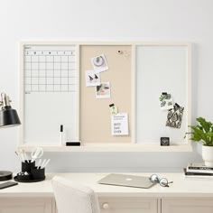 a white desk topped with a laptop computer next to a wall mounted calendar and pen