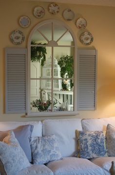 a white couch sitting under a window next to a table with plates on top of it