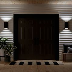 a black door with three lights on it in front of a white wall and wooden floor