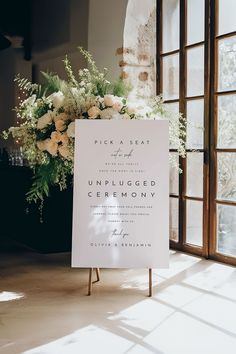 an unplugged ceremony sign sitting in front of a window with flowers on it