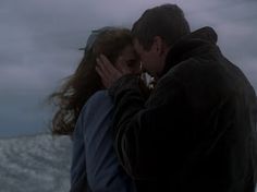 a man and woman kissing in front of snow covered mountains on a gloomy day