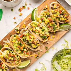 several tacos are lined up on a cutting board next to a bowl of salad