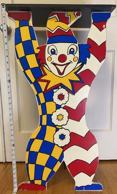 a large wooden clown standing next to a ruler on the floor in front of a door