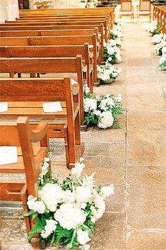 rows of wooden pews with white flowers on the floor and in between them are empty chairs