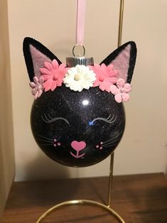 a black cat ornament with pink and white flowers on it's head