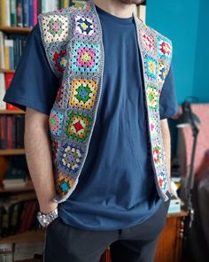 a man standing in front of a bookshelf wearing a crocheted vest