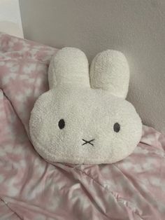 a white stuffed animal laying on top of a pink comforter next to a wall