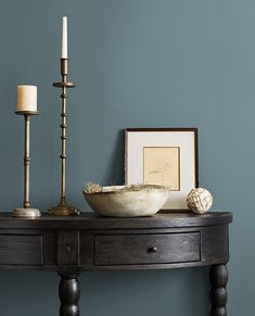 a wooden table with a bowl and two candles on it next to a framed photograph