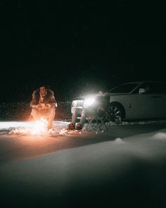 two people sitting around a campfire in the dark with one person holding a flashlight