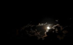 the moon is shining brightly in the night sky with clouds and dark skies behind it