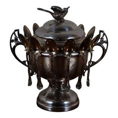 an ornate silver pot with spoons and forks on it's lid, set against a white background