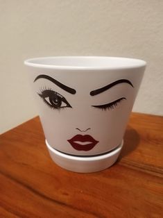 a white cup with a face painted on the side sitting on top of a wooden table