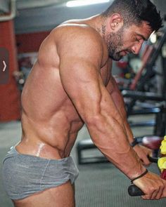 a shirtless man holding a barbell in his hand and looking down at the ground