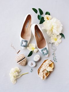 wedding shoes and accessories laid out on a white surface with flowers in the foreground