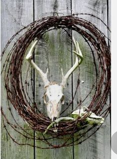 a deer skull is mounted on a wreath made out of branches and barbed wire, against a wooden fence