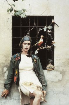 a woman sitting on the side of a building next to a window with birds in it