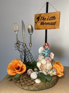 there is a sign that says the little mermaid with shells and seashells around it