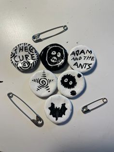 six buttons with black and white designs are on a table next to two pins that say, the cup and the ants