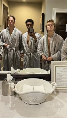 four men in robes taking a selfie with their cell phone while standing in front of a bathroom mirror