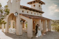 a bride and groom standing in front of a church with an outdoor ceremony area behind them