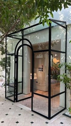 a black glass house sitting on top of a tiled floor next to a lush green tree