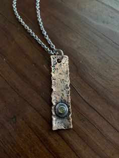 "This pendant is hand forged from thick, rustic bronze. It is accented with a reclaimed Sterling silver nugget and a small, 4mm natural peridot gemstone. Pendant comes with a 20\" closed link surgical stainless steel chain. This necklace is unisex in design and perfect for layering or wearing alone. Peridot is the traditional birthstone for those born in the month of August. MEASUREMENTS & SPECIFICS: PENDANT LENGTH: 5CM PENDANT WIDTH: 12MM NECKLACE LENGTH: 20\" NECKLACE MATERIAL: high qualit Rustic Bronze Electroformed Jewelry, Rustic Hand Forged Bronze Jewelry, Rustic Silver-colored Brass Jewelry, Rustic Silver Brass Jewelry, Unique Stamped Bronze Jewelry, Artisan Stamped Brass Jewelry, Nature-inspired Hammered Pendant Necklace, Rustic Bronze Soldered Necklace, Artisan Metal Jewelry With Stamped Details