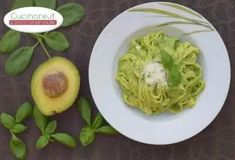 an avocado and pasta dish on a white plate with leaves around the bowl