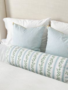 two pillows sitting on top of a bed with white sheets and blue striped pillow cases