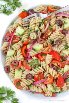 a white bowl filled with pasta salad next to a fork and parsley on the side