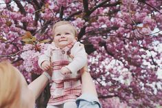 a woman holding a baby up in front of a tree with pink flowers on it