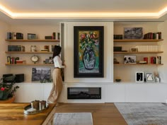 a woman standing in front of a painting on a wall next to a fire place