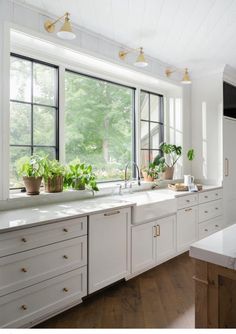 a kitchen filled with lots of white counter top space next to a window covered in potted plants