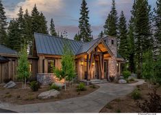 a small cabin style home surrounded by pine trees and rocks in the evening light with a pathway leading to it