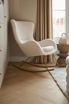 a white rocking chair next to a window in a living room with beige drapes on the windowsill