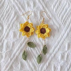 two crocheted flowers are hanging from earrings on a white sheet with green leaves