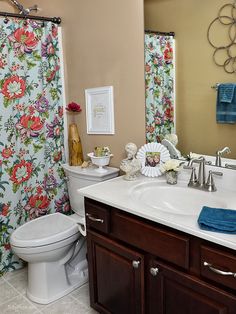 a bathroom with a sink, toilet and shower curtain covered in floral fabric on the walls