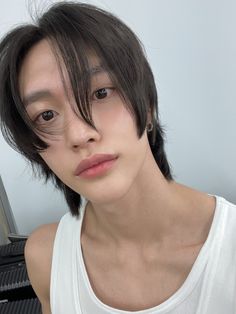 a young man with dark hair wearing a white tank top and looking at the camera