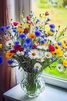 a vase filled with lots of colorful flowers on top of a table next to a window