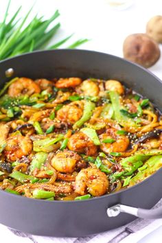 shrimp and asparagus stir fry in a skillet on a white surface with green onions