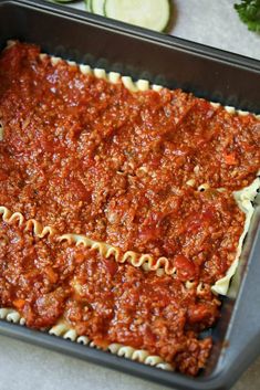 an uncooked lasagna casserole dish in a baking pan with cucumbers on the side