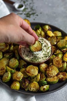 a person dipping some kind of sauce on top of roasted brussel sprouts