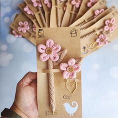 a person holding up some pink flowers in front of brown paper bags with tags attached to them