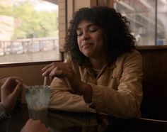 a woman sitting at a table with a drink in front of her and another person standing next to her