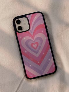 a pink and purple heart phone case sitting on top of a white sheet covered bed