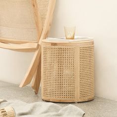 a wicker side table with a glass on it next to a chair and towel