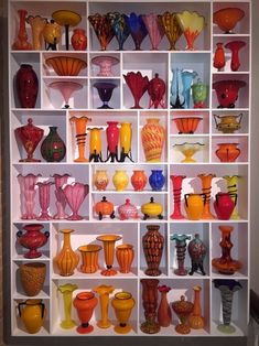 many different colored glass vases on display in a white shelf with shelves behind them