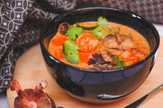 a black bowl filled with soup on top of a wooden cutting board next to a knife and fork