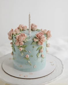 a birthday cake decorated with pink flowers and a single candle on a white tablecloth