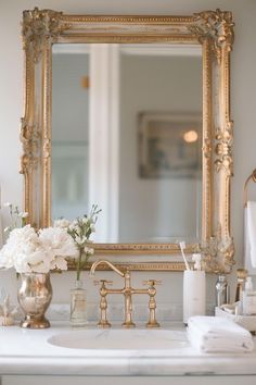 a bathroom sink with a mirror above it and flowers in the vase on the counter