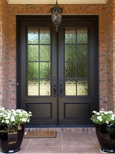 two large black pots with white flowers in front of a double door and entry way